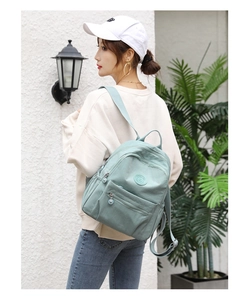 Rear view of a light green nylon mini backpack worn by a model in a casual garden setting