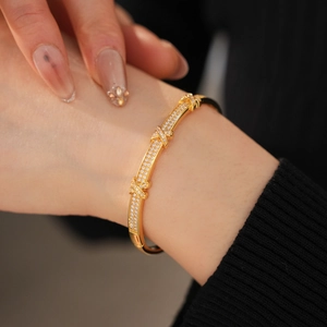 Macro detail of 18k gold plated X-shaped clasp bangle with pavé-set sparkling zircons