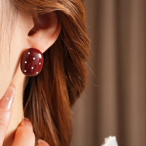 Dettaglio di orecchini ovali rosso vino a pois bianchi indossati da una modella