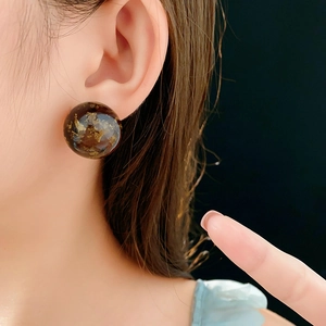 Close-up of deep brown resin round stud earring with gold leaf flakes on ear