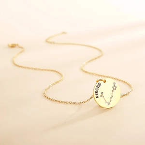 Detail of gold circular Pisces pendant with engraved text and shimmering crystal stones