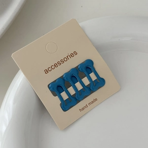Detailed view of three blue bone-shaped mini hair clips on a card inside a ceramic bowl
