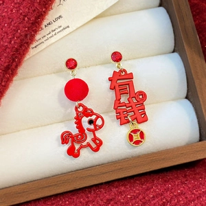 Macro shot of asymmetric festive red earrings with lion and bow charms on velvet background