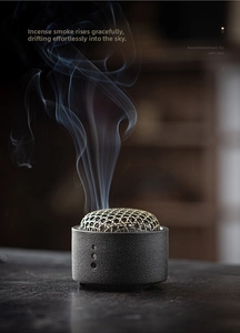 Zen ceramic incense burner with golden hollow lid and wispy smoke on dark wood