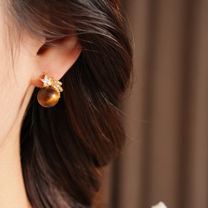 Vue macro d'une boucle d'oreille en œil de tigre avec étoile dorée portée par un mannequin