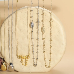 French vintage 14K gold cross necklaces and bow bracelets on a textured stone display