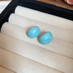 Macro shot of blue marble pattern resin stud earrings on premium beige linen cushion