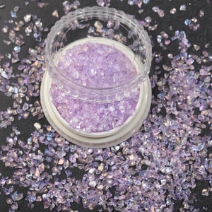 Macro shot of iridescent purple nail art glitter flakes in a clear plastic jar container