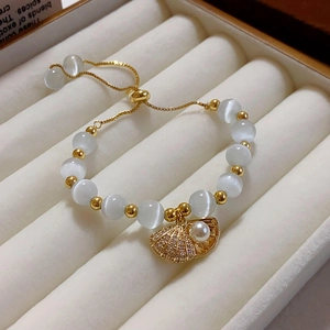 Detailed macro view of gold shell charm with pearl and cat-eye beads on adjustable bracelet