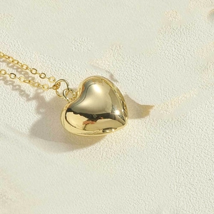 Close-up of polished gold heart pendant necklace on a textured stone background