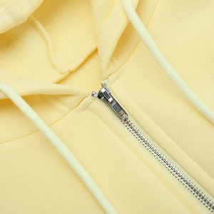 Detailaufnahme des Metallreißverschlusses und der Stricktextur des hellgelben Kapuzenpullovers