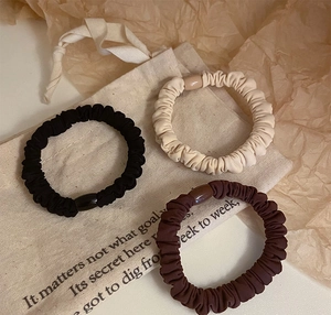 Close-up of three neutral fabric scrunchies in black, beige, and brown on a canvas bag