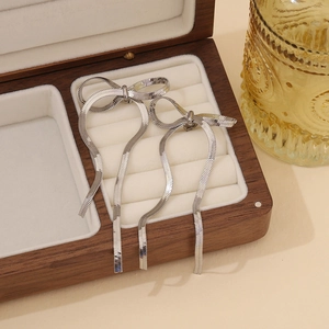 Silver bow tassel earrings on beige velvet lining inside a wooden jewelry box