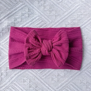 Detailed view of deep pink cable-knit nylon baby headband with a large bow detail