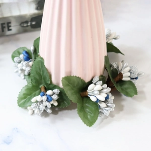 Christmas wreath with white and blue berries and green leaves on a pink fluted vase