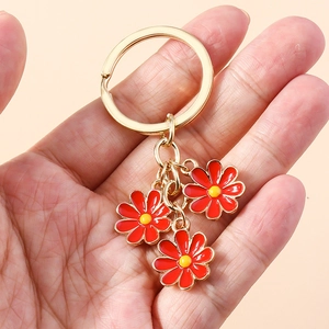 Detailed close-up of golden daisy keychain with red enamel flowers and yellow centers