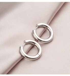 Macro detail of silver stainless steel hoop earrings on elegant pink silk fabric