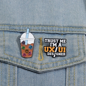 Close-up of enamel pins featuring Adobe icons and UX UI designer text on denim