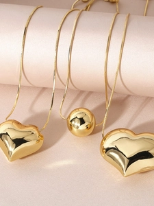 Detail of gold-plated heart and ball pendants on sleek snake chains with mirror finish