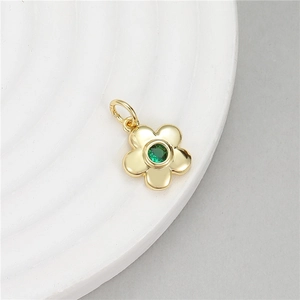 Pendentif fleur dorée à cinq pétales avec pierre verte sur un plateau blanc