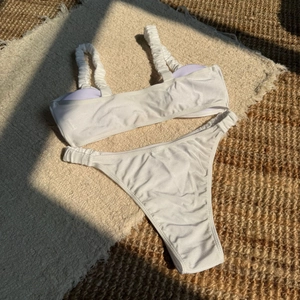 Detail of white ruched bikini set with glossy nylon fabric on a textured summer background