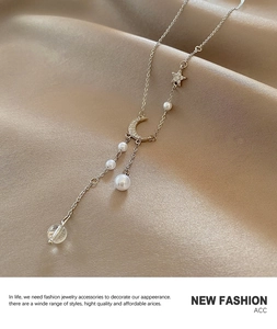 Macro view of moon pendant and star charm on silver tassel necklace over silk fabric