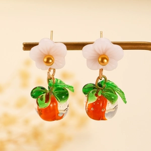 Detailed view of orange fruit earrings with white flowers and green leaves on gold stand