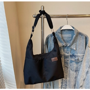 Detail of a large black canvas tote bag hanging next to a blue denim jacket