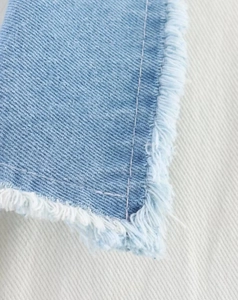 Close-up of light blue denim fabric featuring reinforced double stitching and frayed edges