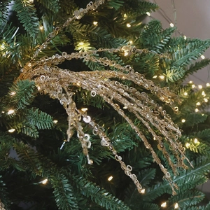 Sparkling gold sequin branch ornaments on a Christmas tree with warm LED lights background
