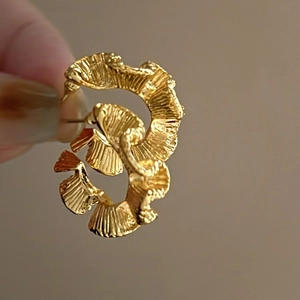 Detailed view of gold twisted metal earring with wavy fan-shaped texture and refined finish