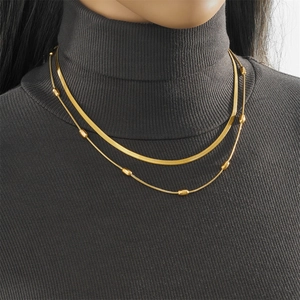 Détail d'un collier double rang doré avec chaîne serpent et perles sur un pull gris