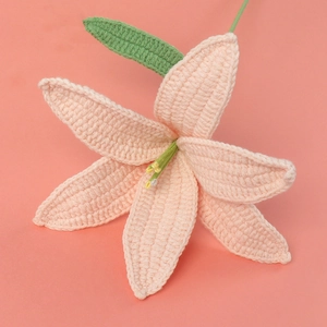 Close-up of a handmade pink crochet lily with green leaf on a matching background