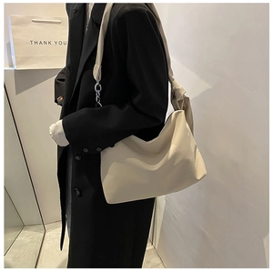 Detail of cream crossbody bag with knot strap detail worn over a black winter coat