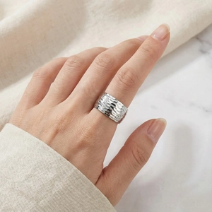 Close-up of a silver wide band ring with a hammered metal texture worn on a finger