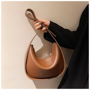 Détail d'un sac porté épaule en cuir marron en forme de croissant tenu par un mannequin chic