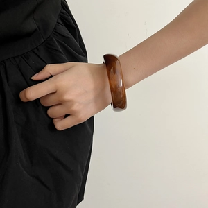 Detail of amber translucent resin bangle with marble texture on wrist against a white wall