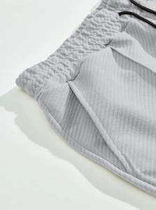 Detail of light gray ribbed knit trousers showing elastic drawstring waist and side pockets