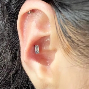 Gros plan d'un clou d'oreille en titane G23 avec cristal rectangulaire sur le cartilage