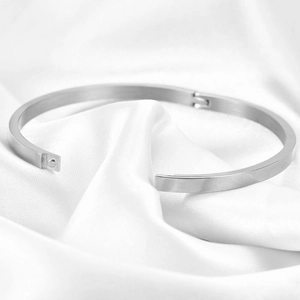 Detailed close-up of a silver stainless steel 4mm flat bangle on white soft fabric background