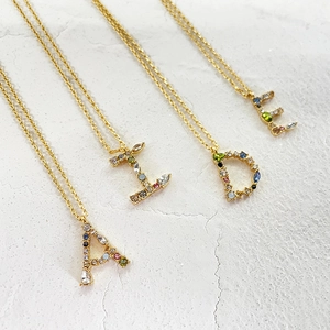 Detail of 18k gold initial necklaces A, I, D, E with colorful zircons on a white background