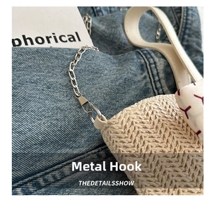 Detail of metal hook and chain strap on a white straw tote bag with denim background