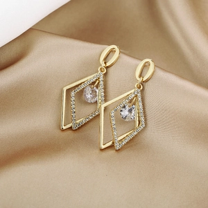 Close-up of golden geometric diamond-shaped earrings with crystals on champagne satin fabric