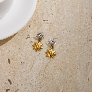 Close-up of two-tone sun and star drop earrings on a neutral stone background