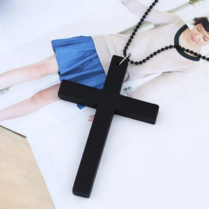 Close-up of a large black cross necklace featuring a beaded chain on a magazine background