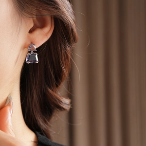 Close-up of purple zircon earrings with triangle and square gems worn by a model