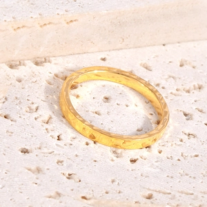 Close-up of golden stainless steel ring with hammered texture on a textured stone surface