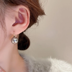 Close-up of a dark grey pearl earring with gold hook worn by a model in soft lighting