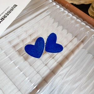 Close-up of blue flocked heart-shaped stud earrings with velvet texture on clear board