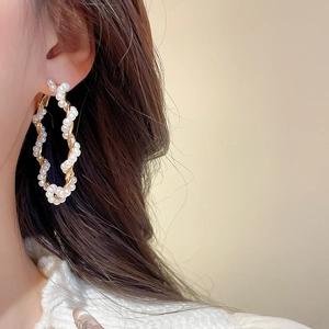Detailed close-up of a gold twisted hoop earring with white pearls worn by a model